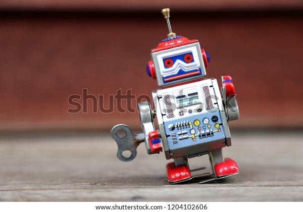 A vintage wind up toy robot, on a blurred\
wood background.