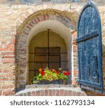 Vintage window in the old Fredrikstad city in Norway with a blue shutter on old brick wall. The house is from the 1700-1800 century. Flowers and iron grilles in front of the window in the opening. 