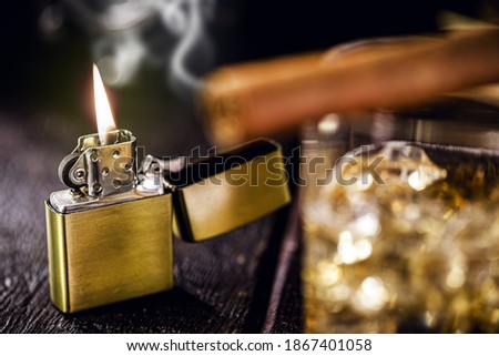 vintage windproof lighter on rustic wooden background. Access cigar and glass of alcohol in front, spot focus