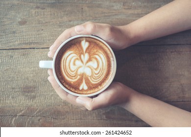 Vintage woman hands holding latte art coffee mug on old wooden background