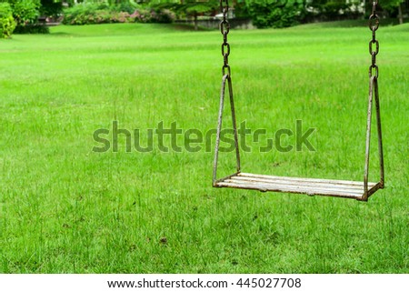 A vintage wood swing hanging over green grass in the playground