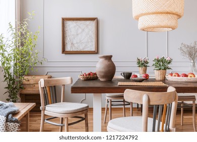 Vintage wooden chairs in living room with long table with strawberries, apples, vase and flowers on it, real photo