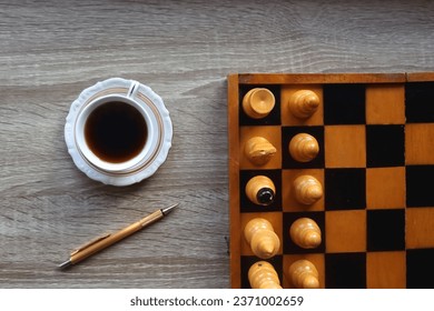 Vintage wooden chessboard, books, glasses, pen, cup of tea or coffee and scented candle on the table. Dark academia concept. Top view.