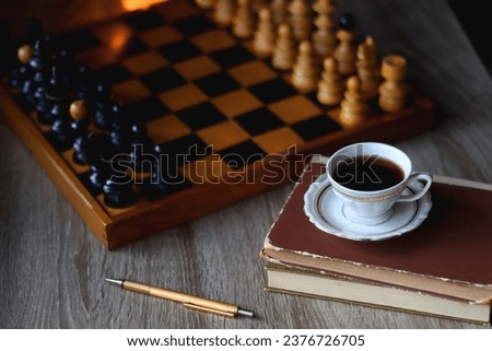 Vintage wooden chessboard, books, glasses, pen, cup of tea or coffee and scented candle on the table. Dark academia concept. Selective focus.