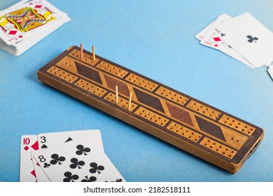 Vintage Wooden Cribbage Board And Playing Cards On Blue Background. Cribbage Is A Classic Fast Scoring Card Game With A Board And Pegs To Keep Score. Its Origins Date From The 17th Century.