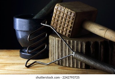 VINTAGE WOODEN MALLET AND METAL MASHER WITH A WOODEN KITCHEN BLOCK AND A BLACK MARBLE PESTLE AND MORTAR