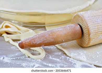 A Vintage Wooden Rolling Pin, Pie Plate With Raw Pie Crust In It, Cut Crust And Flour On A Baking Mat.