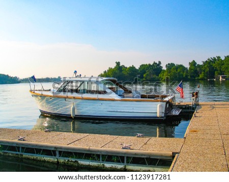A vintage wooden sea skiff boat with an American flag on the back moored at a dock in a lake with reflection an bouys and trees on the opposite bank