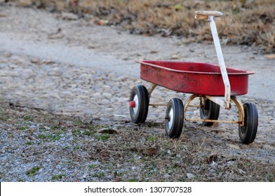 Vintage, worn little red wagon alone on a gravel road 