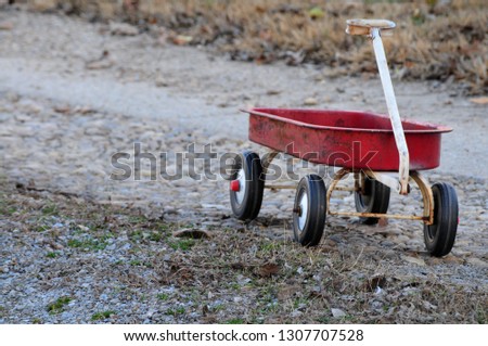 Vintage, worn little red wagon alone on a gravel road 