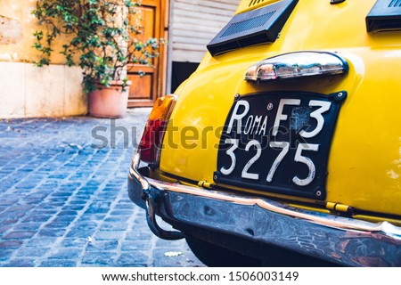 Vintage yellow car in the street with an old car plate in Rome.