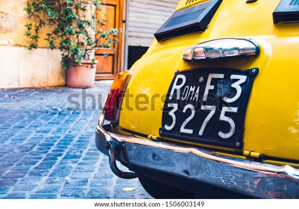 Vintage yellow car in the street with an old car\
plate in Rome.