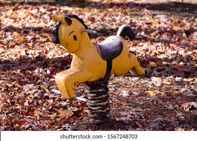 Vintage, yellow, spring rider rocking horse on coils, standing proud despite chipped paint and rusty coils; awaiting the next generation of eager children to bring laughter to the fall sunshine. 