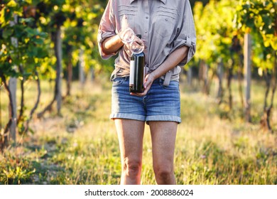Vintner holding red wine bottle and drinking glass in vineyard. Woman winetasting outdoors - Powered by Shutterstock