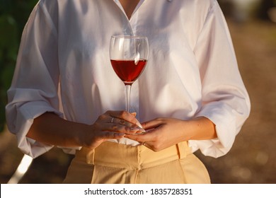 Vintner Woman Tasting Red Wine From A Glass In A Vineyard. Vineyards Background At Sunset. Macro Shot Of A Sommelier Hand That Hold The Wineglass