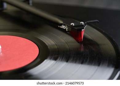 Vinyl player.
				The tonearm with the stylus is mounted on a black spinning vinyl record. Red cartridge