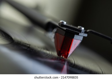 Vinyl player.
				The tonearm with the stylus is mounted on a black spinning vinyl record. Red cartridge