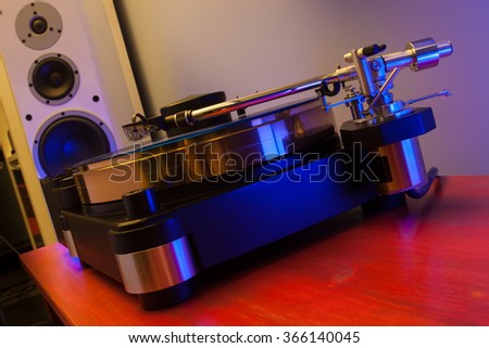 Vinyl record played on a hi-end turntable record player standing on red wood stand with speakers on background