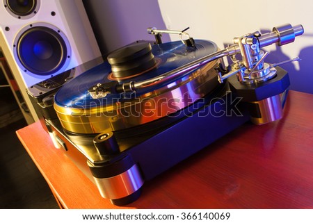 Vinyl record played on a hi-end turntable record player standing on red wood stand with speakers on background 