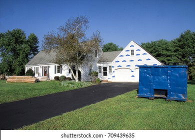 Vinyl Siding Supplies Packaged And Sitting In Front Of Home Ready To Replace Existing Siding On House.  Large Commercial Dumpster Next To House Ready For All Debris And Old Siding To Be Placed.