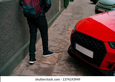 Violation of traffic rules. A guy walking on the pavement where red car parked too close to the building. Sidewalk