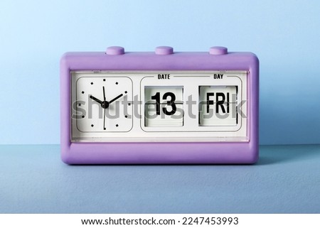 Violet alarm clock placed on table against blue wall set for Friday 13th