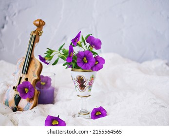 Violet flowers with violin toy on white embroidered cloth for background, Calibrachoa petunia Million bells ,Trailing petunia ,Superbells ,seashore smaller flowers ,Solanaceae ,still life creative 