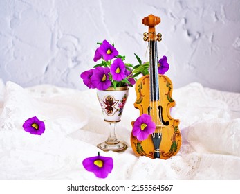 Violet flowers with violin toy on white embroidered cloth for background , Calibrachoa petunia Million bells ,Trailing petunia ,Superbells ,seashore smaller flowers ,Solanaceae ,still life creative 