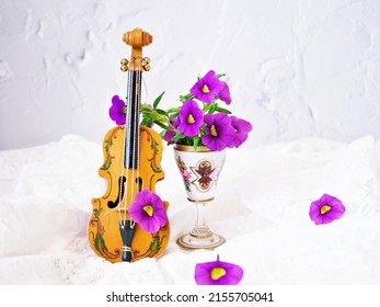 Violet flowers with violin toy on white embroidered cloth for background,Calibrachoa petunia Million bells ,Trailing petunia ,Superbells ,seashore smaller flowers ,Solanaceae ,still life creative