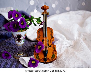 Violet flowers with violin toy on white embroidered cloth for background,Calibrachoa petunia Million bells ,Trailing petunia ,Superbells ,seashore smaller flowers ,Solanaceae ,still life creative