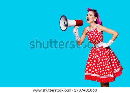 Violet red haired woman using megaphone, shouting something. Girl in pin-up style dress in polka dot isolated over aqua blue color background. Retro fashion vintage studio concept. Copy space for text