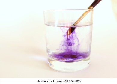 The violet watercolor from an art brush rastovoryatsya in a glass with clear water on a white background - Powered by Shutterstock