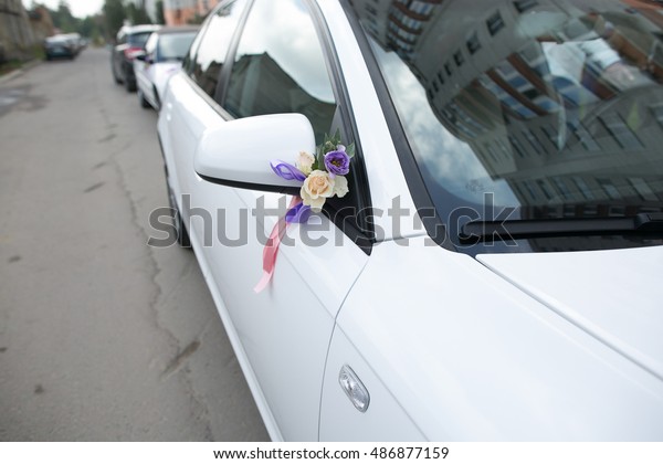 Violet and white flowers pinned to white car\'s\
rare mirror