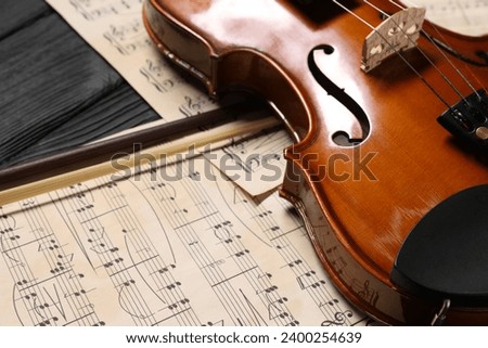 Violin, bow and music sheets on black wooden table, closeup
