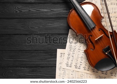 Violin, bow and music sheets on black wooden table, top view. Space for text