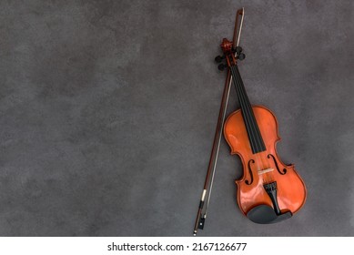 Violin and bow on gray wood background. Flat lay, top view, copy space. Concept of classical music, bowed string musical instrument