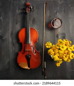 violin, bow, yellow flowers and glass of cognac on black wooden background