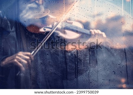 Violin and clasical music concept abstract defocused background.Playing violin song behind the window with water drops on a rainy day. Sad music for travel road.