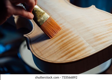 violin maker varnishing a violin body close up. orange brush leaves a wet trace on the wood texture. Atmospheric handmade master work. - Powered by Shutterstock