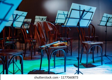 Violin And Music Stand. Violin On A Chair And Music Stands With Notes Around. The Orchestra Is On Break. Sweater On The Back Of A Chair