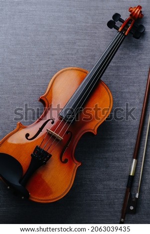 A violin on a grey textile surface. It's in a perfect condition. Next to a bow.