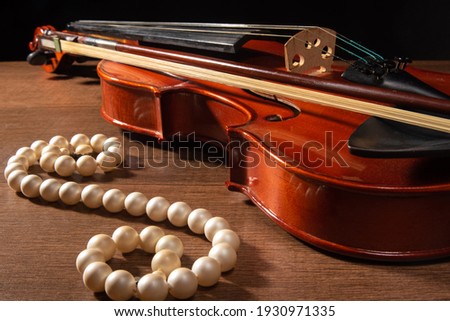 Violin and pearl necklace, arrangement with violin and pearl necklace on wooden surface, low key portrait, selective focus.