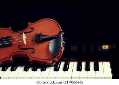 violin placed on a piano on a black background