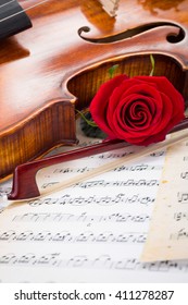 Violin, red rose and bow on musical score