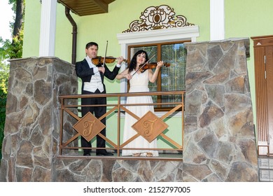 violinist and violinist play violins on the porch of an old house.