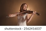 Violinist standing and playing on the classical violin on dark concert stage against golden spotlight, isolated on studio background. Artist in concert hall.