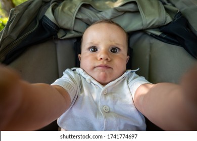Viral close up of newborn baby boy is making a his first selfie or video call to parents or relatives while sitting in a baby stroller.