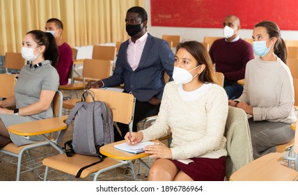 Viral Threat, Seasonal Viral Diseases. Multiethnic Group Of Adult People In Medical Masks Studying Together At Tables In Classroom