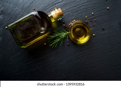 Virgin Olive Oil In A Glass Bottle, Rosemary And Peppercorns On Black Stone Slate, Top View With Blank Space.