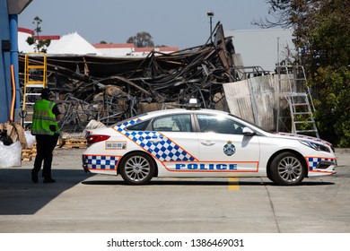 VIRGINIA, QUEENSLAND - SEPTEMBER 24, 2017: A Queensland Police Service Officer Stands Near A Police Car In Front Of The Rubble Of A Large Industrial Factory Fire.